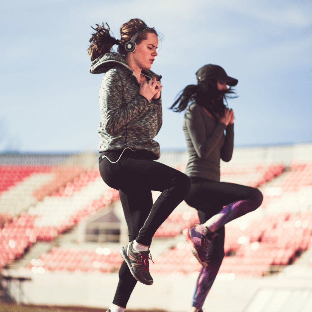 Two young women performing high knees exercise outdoors as part of a HIIT circuit training session, aimed at improving cardiovascular endurance and overall fitness.